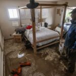 Flooded bedroom with muddy floor and man standing.