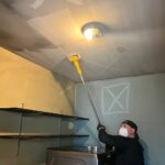 Person cleaning ceiling with mop and protective mask